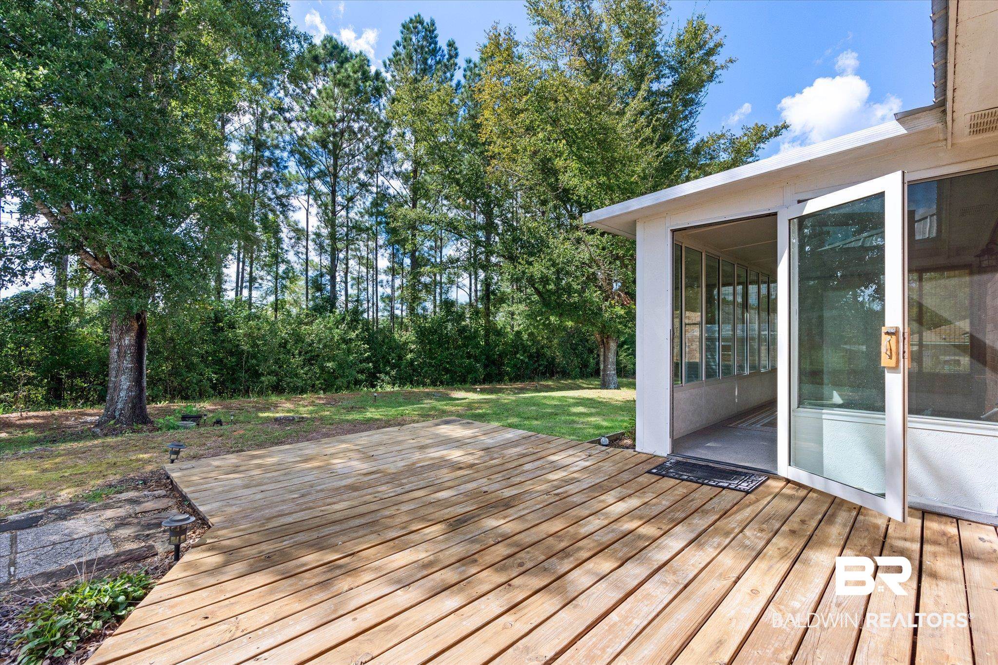 16216 Pointer Drive Foley, AL 36535 - Photo 19 of 21 Expansive wooden deck with a sunroom entry, bordered by a substantial oak tree and dense evergreen foliage