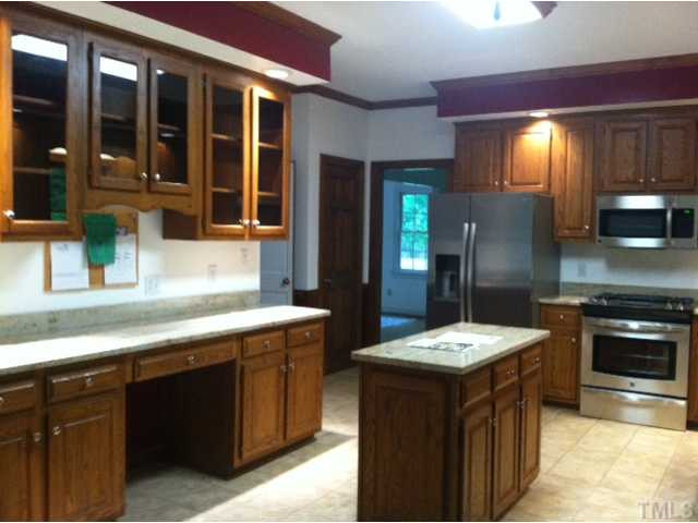 12400 Whartons Way Raleigh, NC 27613 - Photo 5 of 23 Spacious Kitchen with brand new stainless steel appliances. Beautiful granite counter tops.Built in desk area and access to the sun room all overlooking the wooded backyard. Kitchen