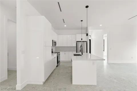 a large kitchen with kitchen island a stove a sink a refrigerator and white cabinets with wooden floor