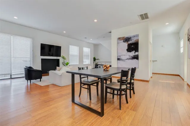 a kitchen with stainless steel appliances granite countertop white cabinets a sink a stove a dining table and chairs with wooden floor