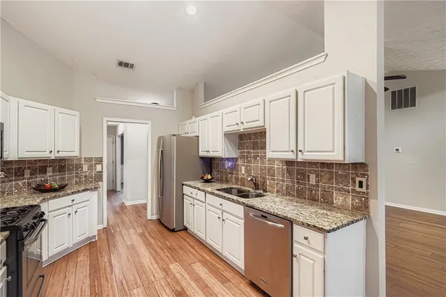 a kitchen with stainless steel appliances granite countertop a stove top oven a refrigerator a sink and dishwasher with wooden floor