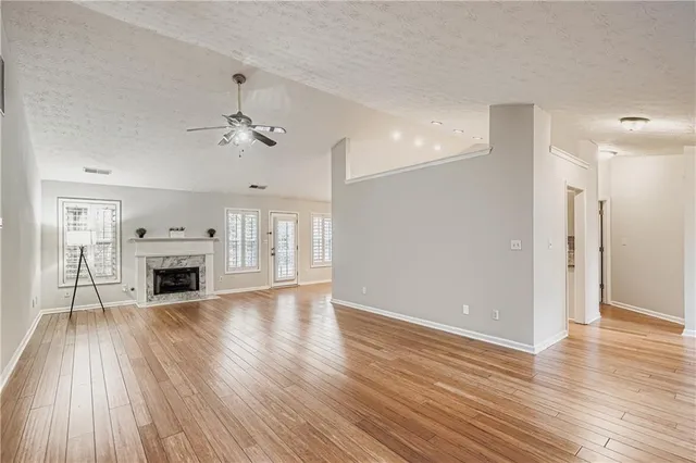 an empty room with fireplace wooden floor chandelier fan and windows
