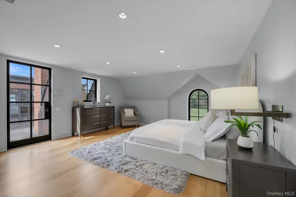 a bedroom with a bed a dresser and potted plants with wooden floor