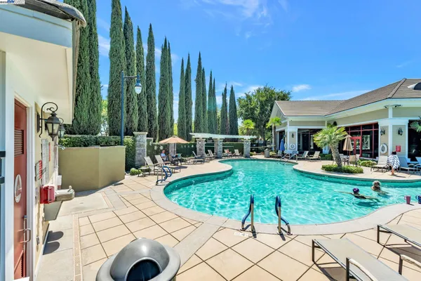 a view of a swimming pool with lawn chairs and large trees