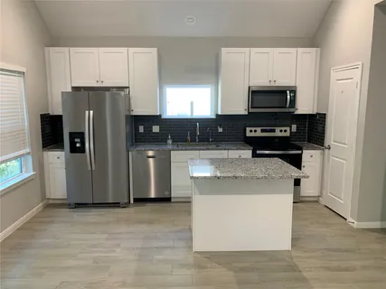 a kitchen with stainless steel appliances granite countertop a stove top oven a refrigerator a sink and dishwasher with white cabinets