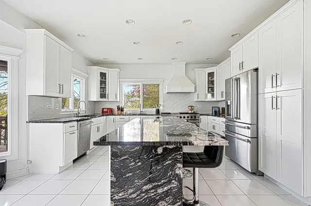 a large kitchen with granite countertop a refrigerator oven a sink a stove and white cabinets