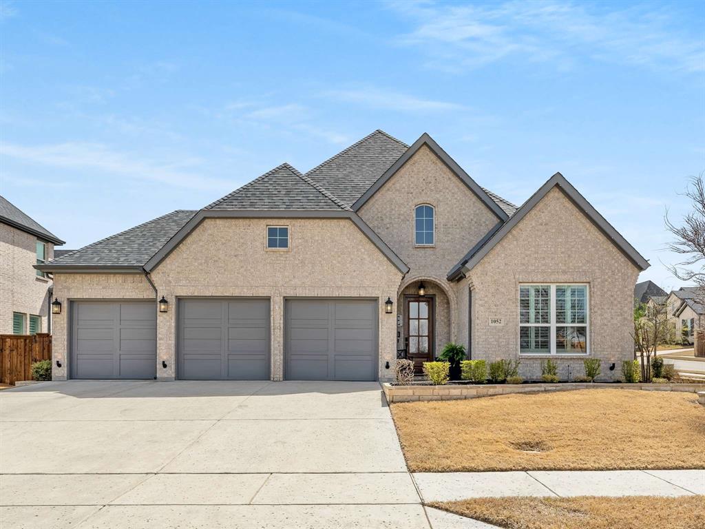 1052 Cabinside Drive Roanoke, TX 76262 - Photo 1 of 1 French provincial home featuring brick siding, an attached garage, a shingled roof, fence, and driveway