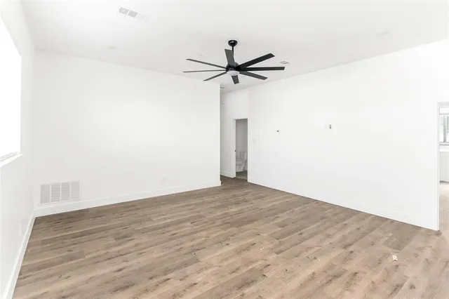 an empty room with wooden floor fan and windows