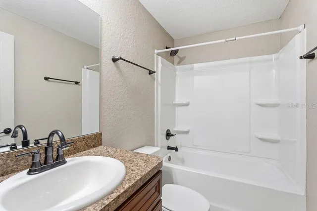 a bathroom with a granite countertop bathtub shower sink vanity mirror and toilet