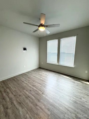 an empty room with wooden floor fan and windows