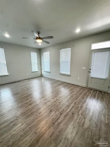 an empty room with wooden floor chandelier fan and windows
