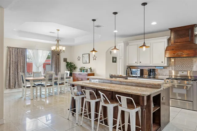 a kitchen with stainless steel appliances granite countertop a stove a sink a center island a refrigerator and a wooden floor