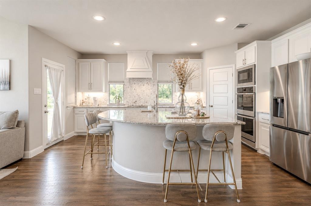 25 Morrison Road Howe, TX 75459 - Photo 8 of 27 Spacious kitchen featuring a large curved island with a light-toned countertop, wood-finish flooring, white cabinetry, and stainless steel appliances