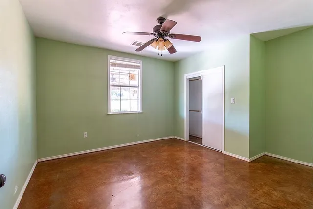 an empty room with a chandelier fan and windows