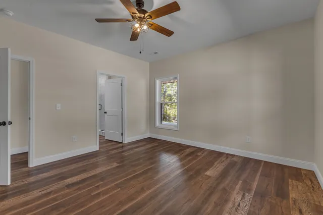 an empty room with wooden floor chandelier fan and windows