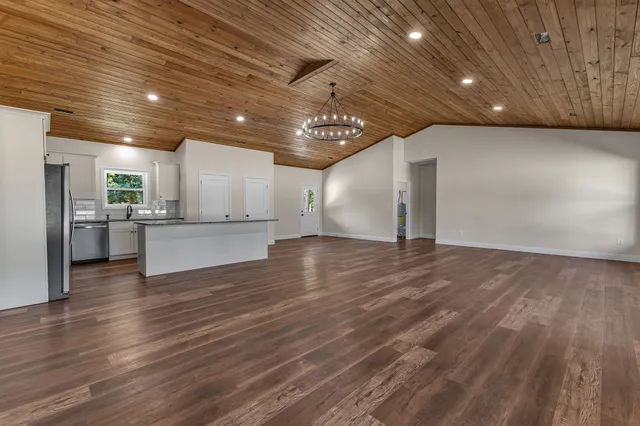 a view of an empty room with wooden floor and a kitchen