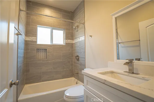 a bathroom with a granite countertop bathtub shower sink vanity mirror and toilet