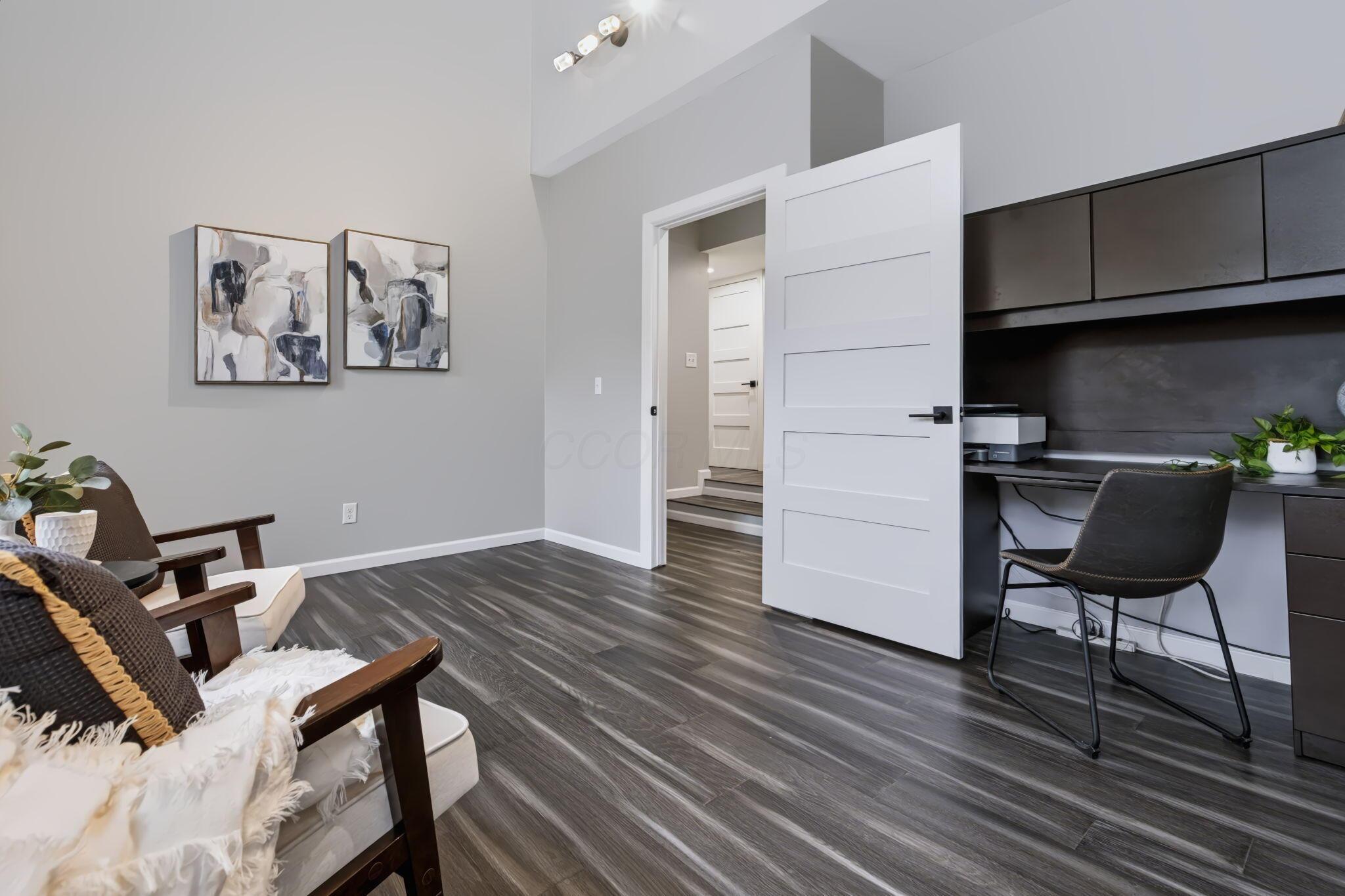 7140 Cook Road Powell, OH 43065 - Photo 74 of 87 Modern studio or open-concept space featuring polished wood-finish plank flooring, clean white architectural details, and a dedicated work zone with built-in dark cabinetry and integrated desk space