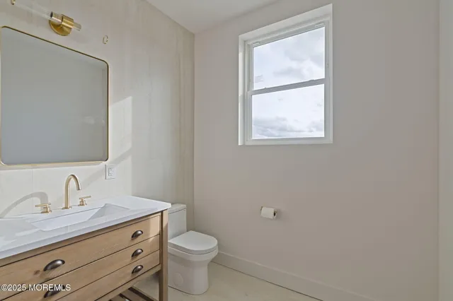 a bathroom with a granite countertop toilet a sink a mirror and a window