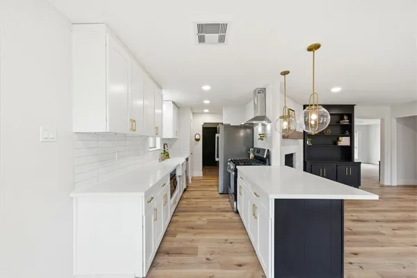 a large white kitchen with a large island oven a stove and white cabinets with wooden floor