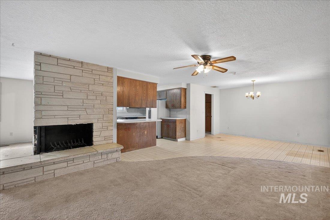10035 W Lane Boise, ID 83709 - Photo 7 of 32 Unfurnished living room with ceiling fan, a stone fireplace, a textured ceiling, light carpet, and hanging lights