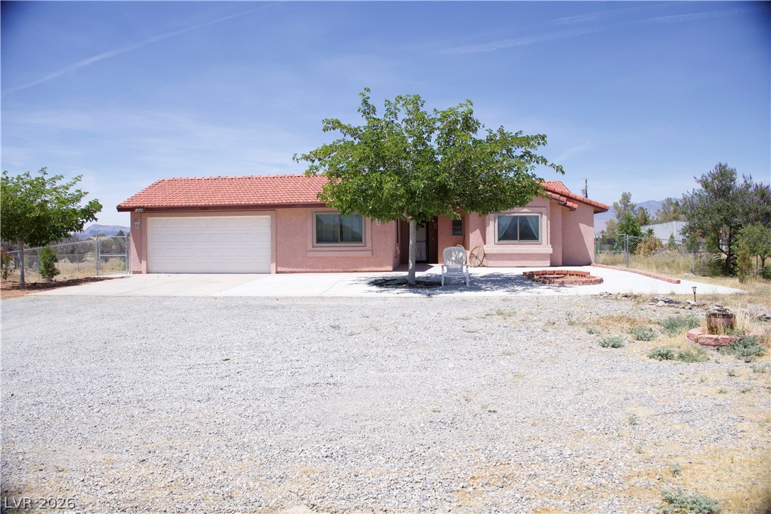 A terracotta-tiled roof crowns this stucco-finished home, complete with an integrated garage and expansive gravel driveway.