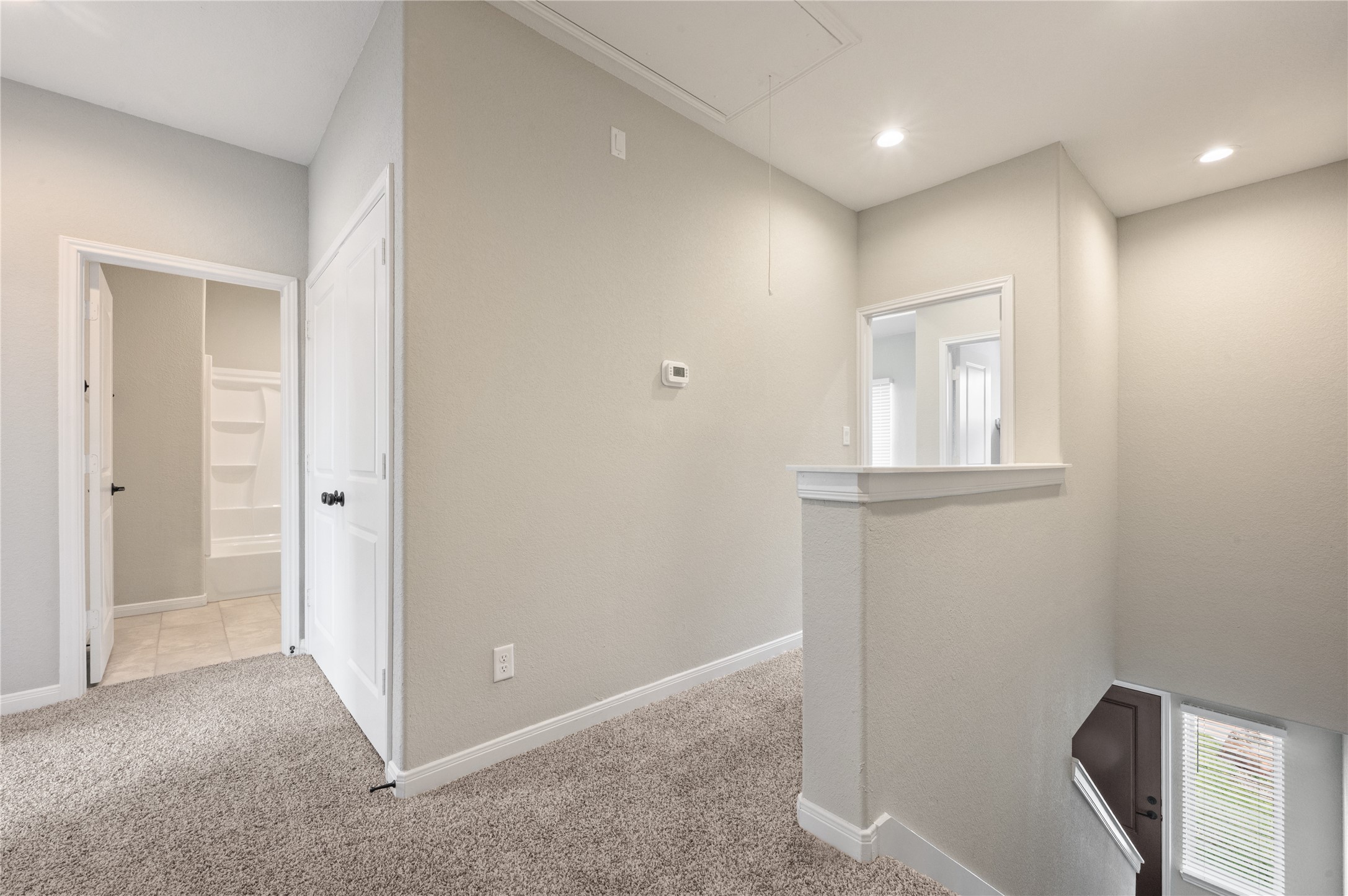 14010 Longstreet Road, Unit 2 Willis, TX 77318 - Photo 19 of 29 This photo shows a well-lit, carpeted hallway with neutral walls. It features a bathroom entrance on the left and a staircase leading downwards on the right. Recessed lighting is installed in the ceiling, adding to the bright and modern feel.
