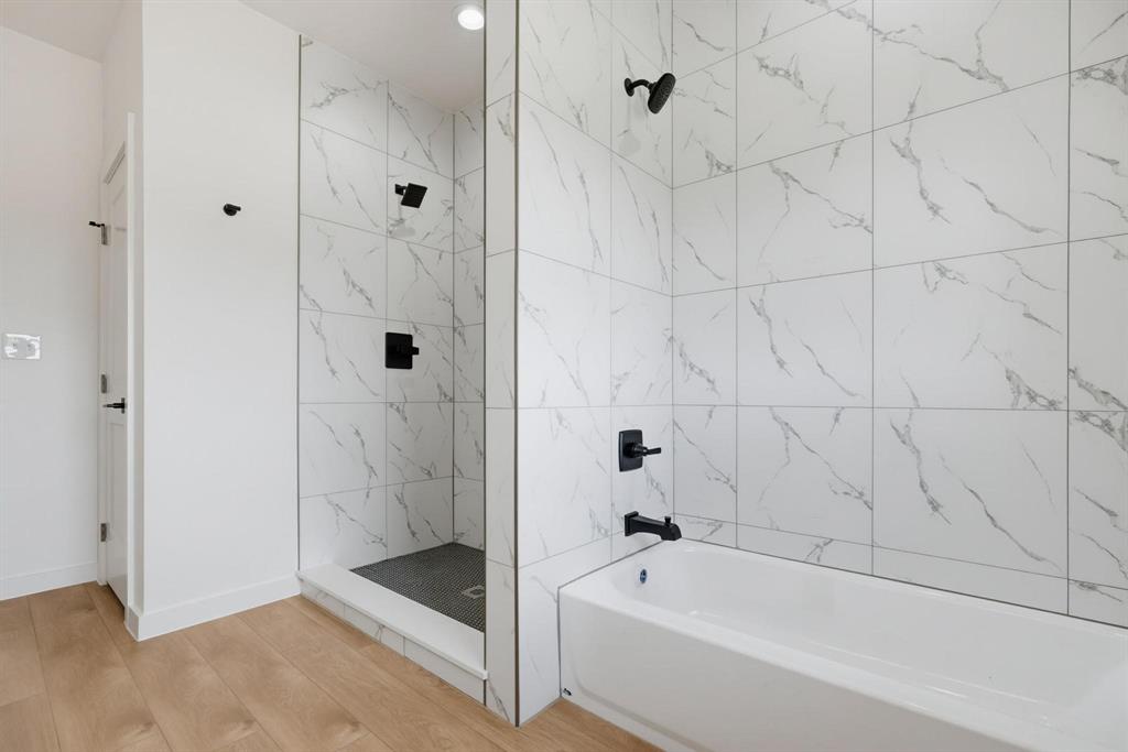 508 South O Connor Road Irving, TX 75060 - Photo 16 of 21 Bathroom featuring a full-sized tub, separate glass-enclosed shower, wood-finish flooring, and white tile walls with veining