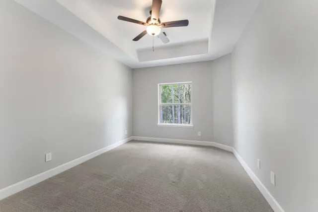 an empty room with chandelier fan and windows