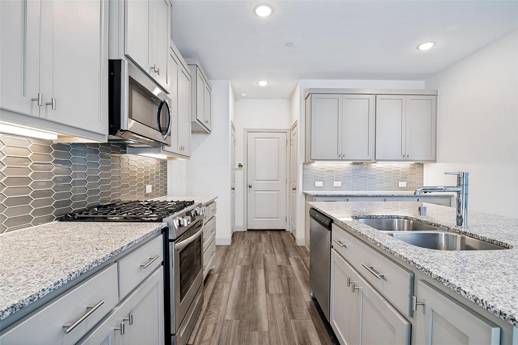 1006 Emil Place Allen, TX 75013 - Photo 11 of 28 Modern kitchen featuring light gray cabinetry with brushed nickel hardware, granite countertops, stainless steel appliances, a gray picket tile backsplash, and wood-finish flooring