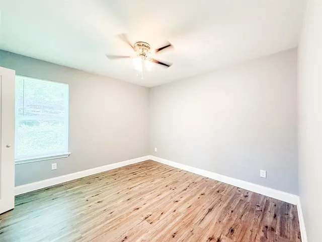an empty room with wooden floor fan and windows