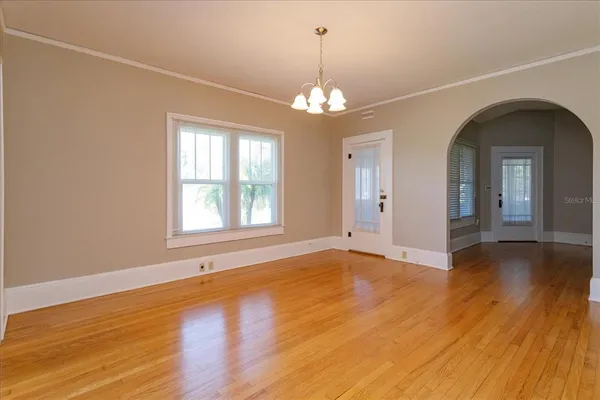 an empty room with wooden floor chandelier and windows