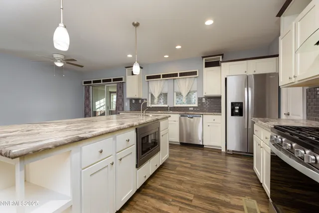 a large kitchen with granite countertop a large counter top a sink stainless steel appliances and cabinets