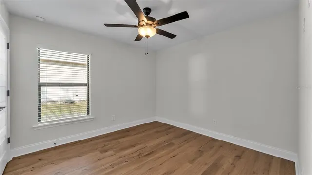 an empty room with wooden floor fan and windows