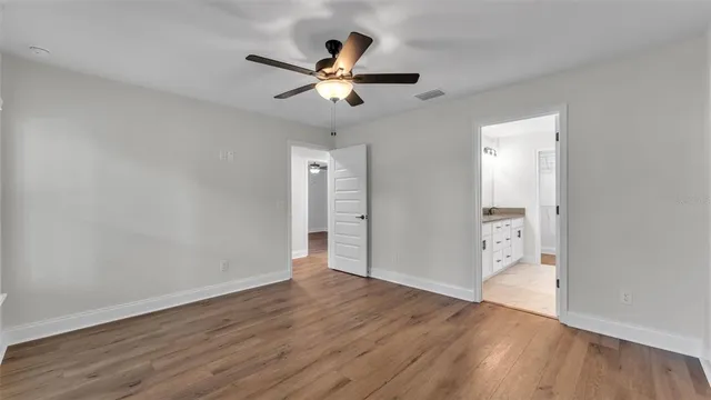 an empty room with wooden floor chandelier fan and windows
