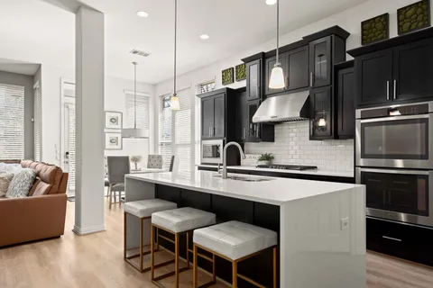 a kitchen with stainless steel appliances granite countertop a sink a stove a refrigerator a dining table and chairs with wooden floor