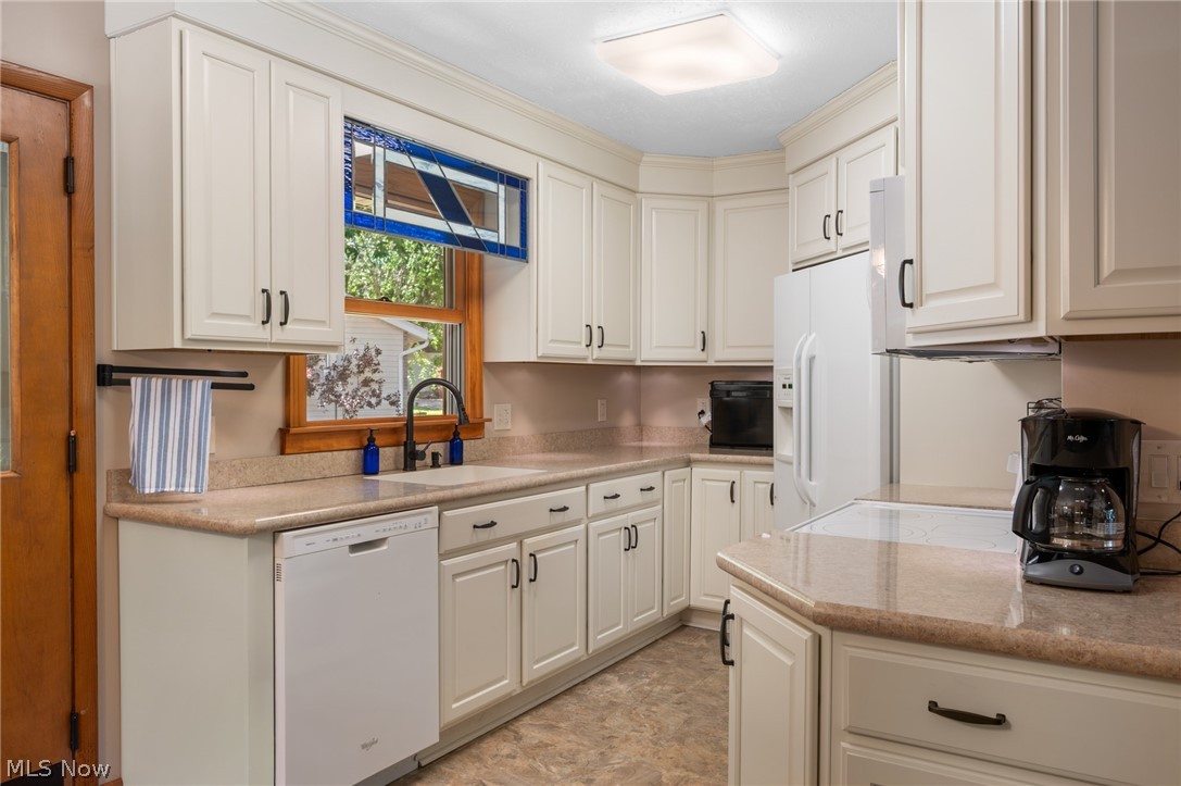 685 Sunnyside Road Vermilion, OH 44089 - Photo 16 of 50 Kitchen featuring white cabinetry, contrasting dark hardware, light-toned countertops, a white dishwasher, and a white refrigerator