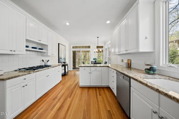 a large kitchen with granite countertop a sink dishwasher stove a refrigerator with white cabinets and wooden floor