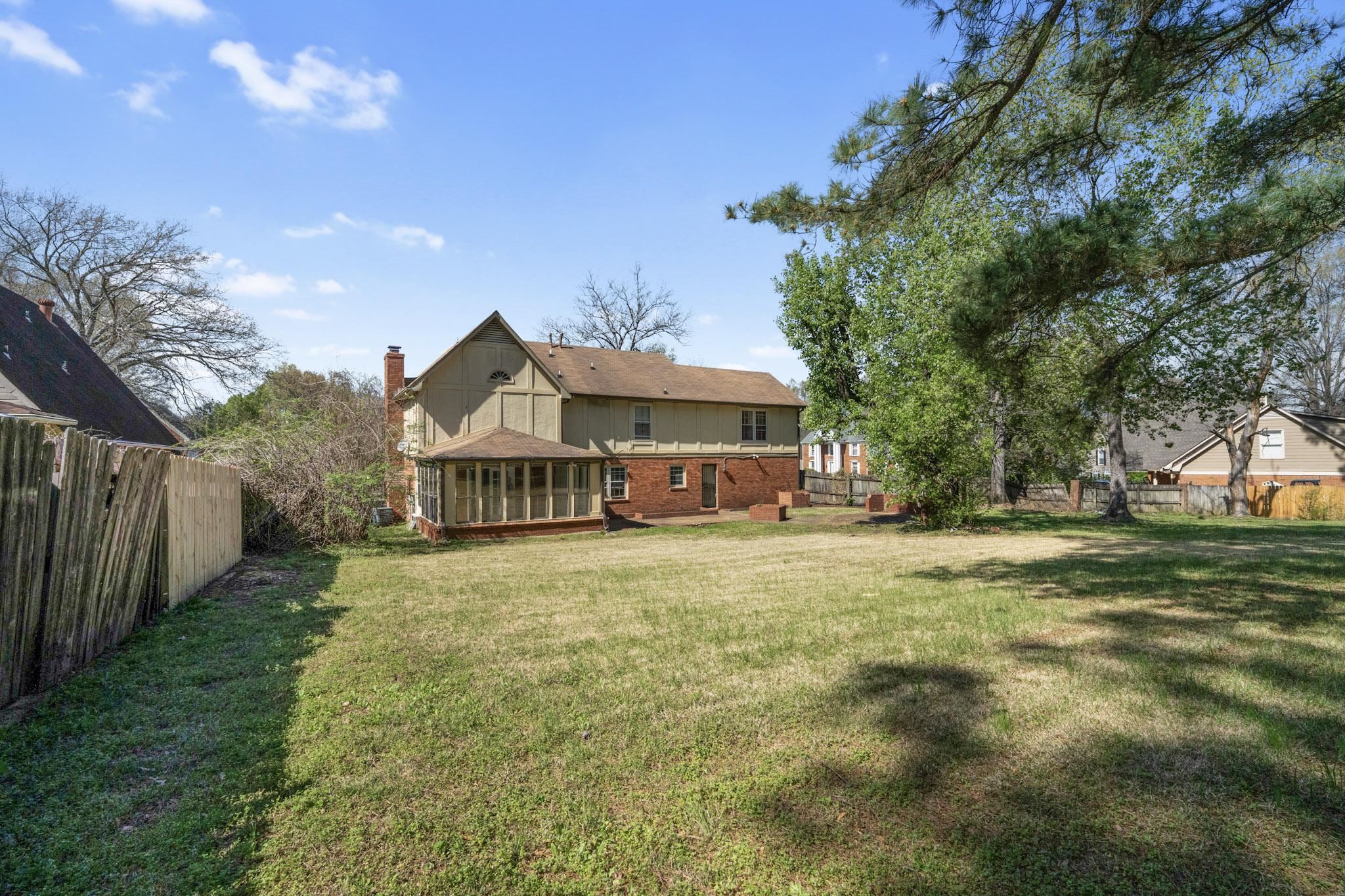 Rear view of property featuring a sunroom, brick siding, a chimney, and a fenced backyard
