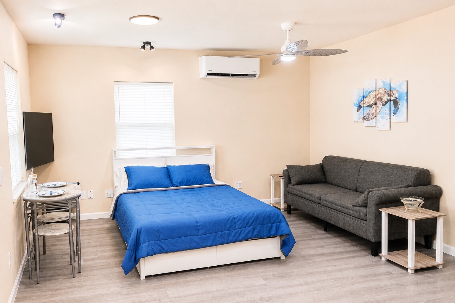 1021 North Sage Road Crystal Beach, TX 77650 - Photo 9 of 22 Bright and cozy bedroom featuring a comfortable bed with blue bedding, a sleek gray sofa, and modern amenities including a wall-mounted TV and air conditioning.
