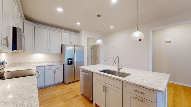 a kitchen with a sink dishwasher a refrigerator and white cabinets with wooden floor