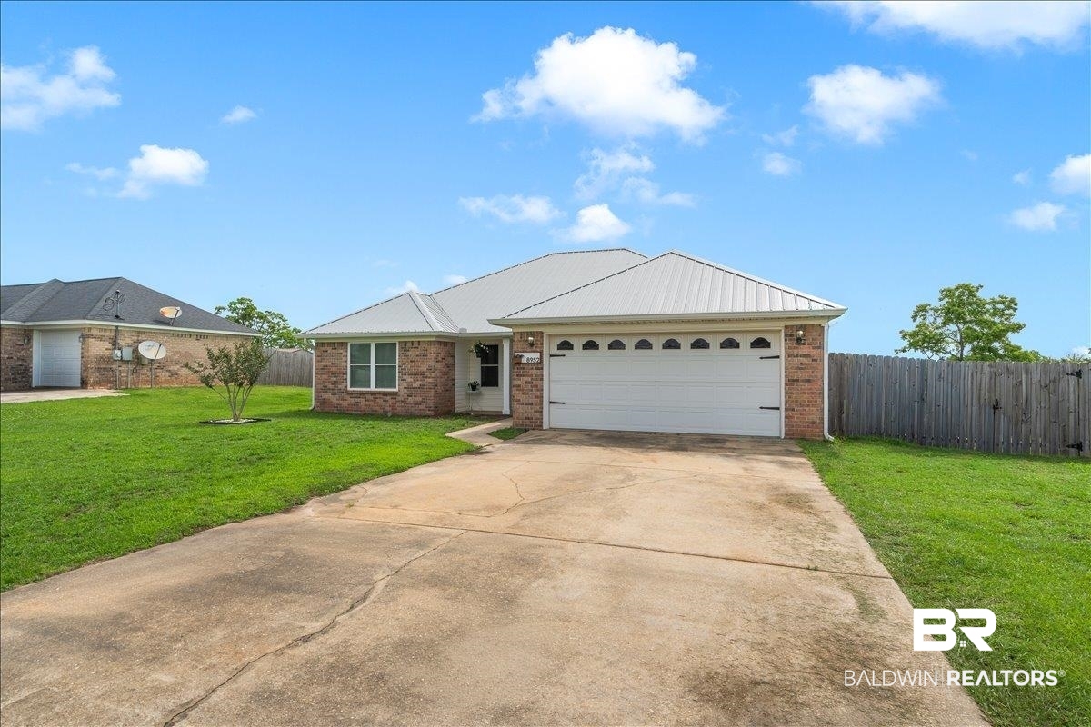 8952 Sherman Road Foley, AL 36535 - Photo 7 of 41 Brick exterior with a metal roof, featuring a two-car garage with decorative windows, a concrete driveway, and a front lawn with a single ornamental tree