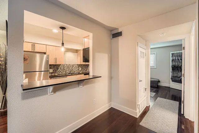 a view of a hallway with wooden floor and a refrigerator in a kitchen