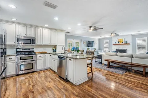 a kitchen with stainless steel appliances granite countertop a stove top oven a sink dishwasher a dining table and chairs with wooden floor