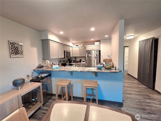 a kitchen with stainless steel appliances granite countertop a refrigerator a stove top oven a sink dishwasher and white cabinets with wooden floor