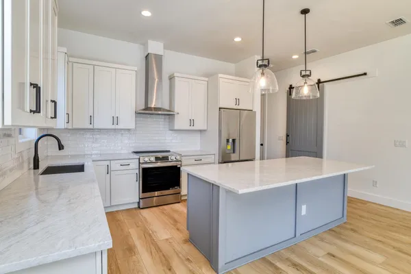 a large kitchen with stainless steel appliances granite countertop a stove a sink dishwasher a refrigerator and white cabinets with wooden floor