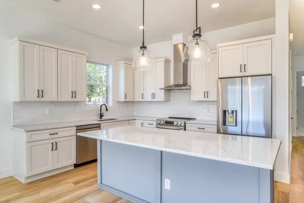 a kitchen with stainless steel appliances granite countertop a sink a stove a refrigerator and island with wooden floor