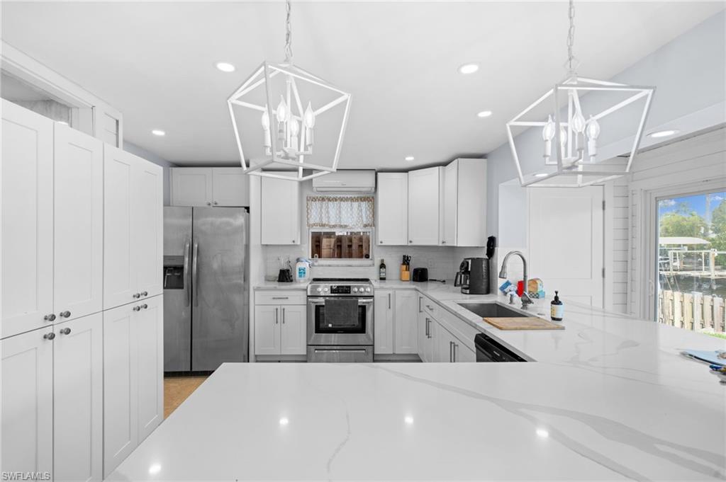 1360 Chesapeake Avenue Naples, FL 34102 - Photo 15 of 22 Kitchen featuring pendant lighting, light stone counters, stainless steel appliances, and white cabinets