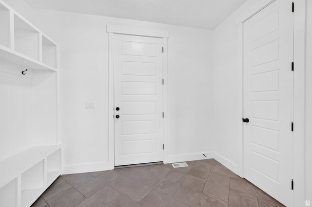 1002 West Temple Rim Lane Payson, UT 84651 - Photo 24 of 68 Built-in white storage bench with cubbies and hooks, complemented by a large white five-panel interior door with black hardware, and dark gray flooring laid in a herringbone pattern