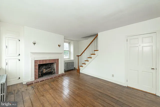 a view of an empty room with wooden floor fireplace and a window